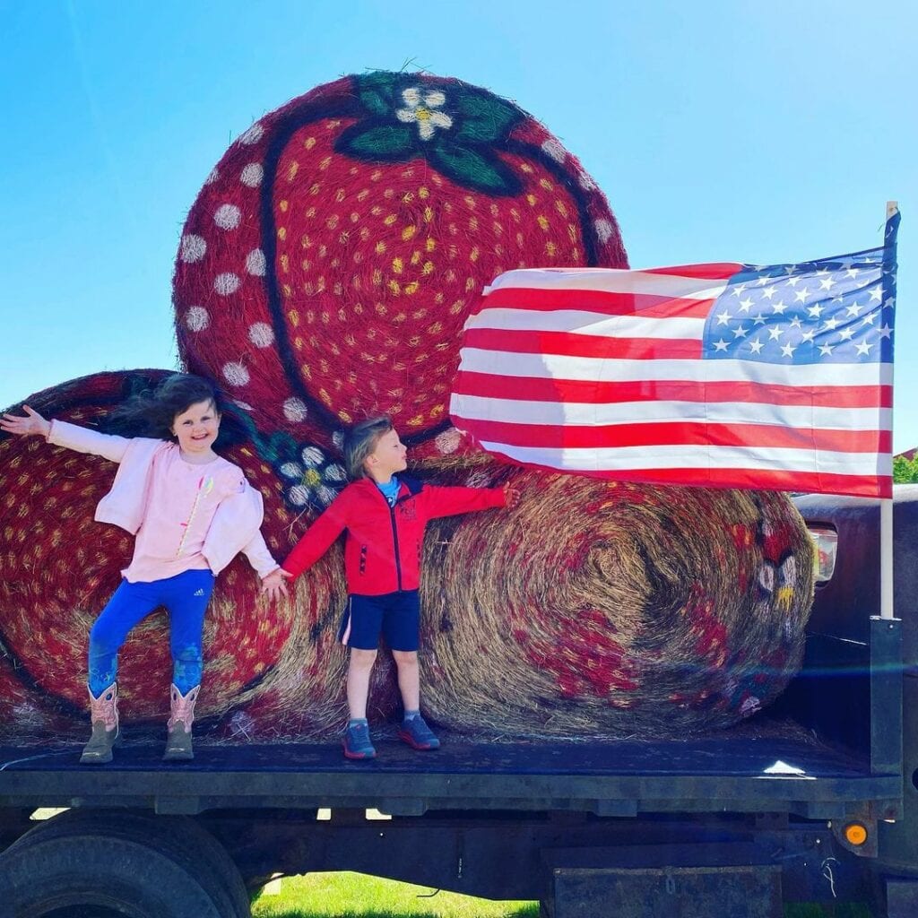 two children on in front of hay bales with American flag